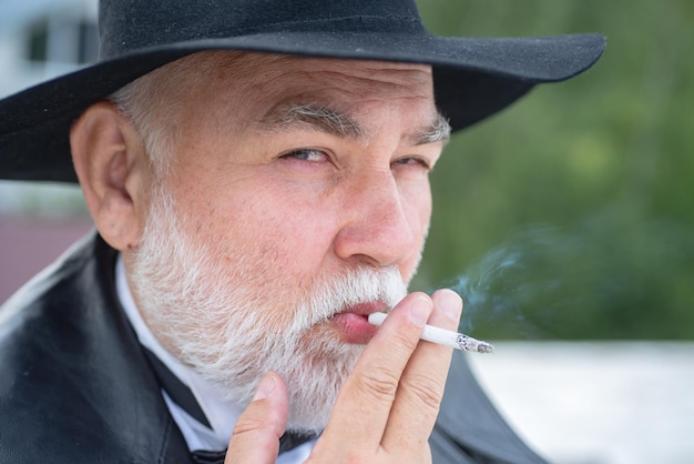 Photo close up portrait of funny stylish hipster grandfather in leather coat smoking outdoor