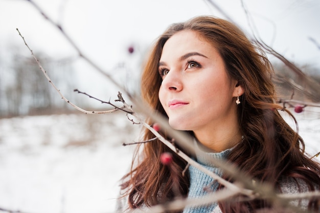 Close up portrait of gentle girl in gray coat near the branches of a snow-covered tree.