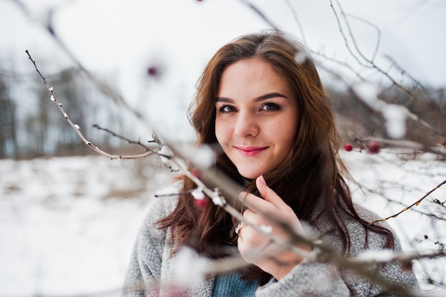 Close up portrait of gentle girl in gray coat near the branches of a snowcovered tree