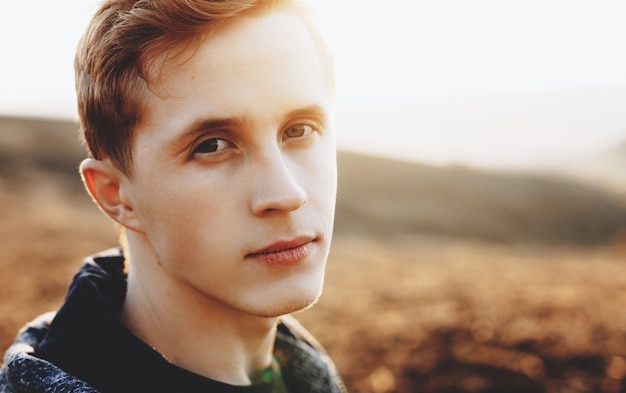 Close up portrait of ginger caucasian man posing in a field while looking at camera