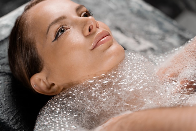 Close-up portrait of girl on foam peeling procedures in spa. Model is relaxing in Turkish hammam.