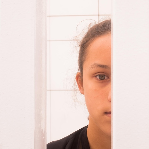Foto ritratto in primo piano di una ragazza che sbircia da una porta aperta.