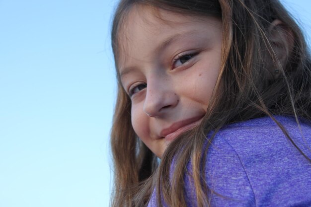 Close-up portrait of girl smiling against sky