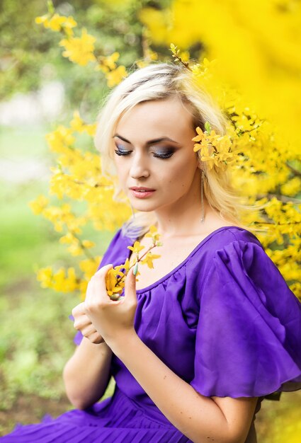 Close-up portrait of a girl with professional makeup. beautiful woman in a purple dress with blooming forsythia.