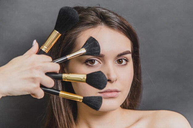close up portrait of gorgeous girl with four makeup brushes she is looking at camera