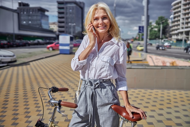 屋外で時間を過ごしながら友人と携帯電話で話しているビジネスカジュアルな服を着たゴージャスな女性の肖像画をクローズアップ