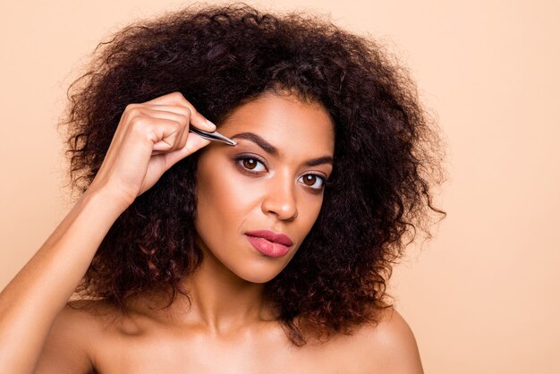 Close-up portrait of gorgeous serious girl using metal forceps styling eyebrow