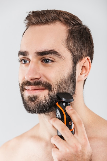 close up portrait of a handsome bearded man shaving with an electric razor isolated over white