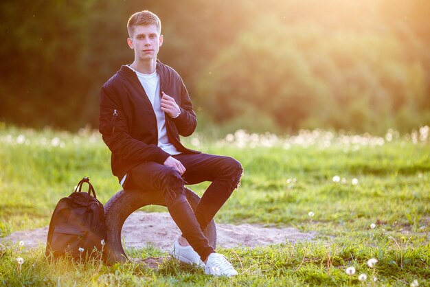 Close up portrait of handsome boy teenager sitting on the stairs in urban street background in the rays of the setting sun