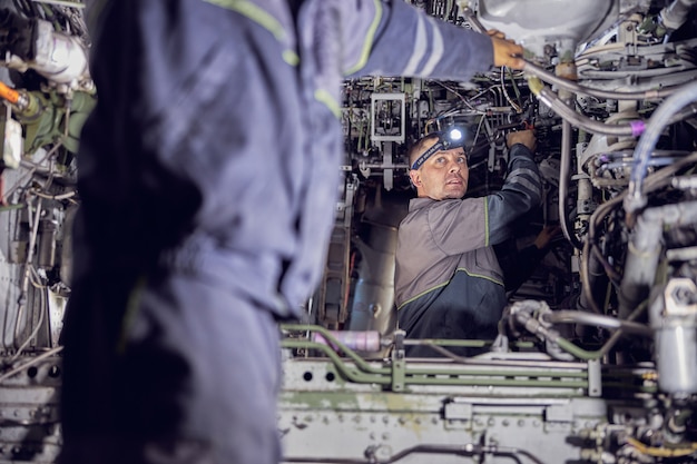 Photo close up portrait of handsome confident male with light on his head while working with inside system of passenger airplane