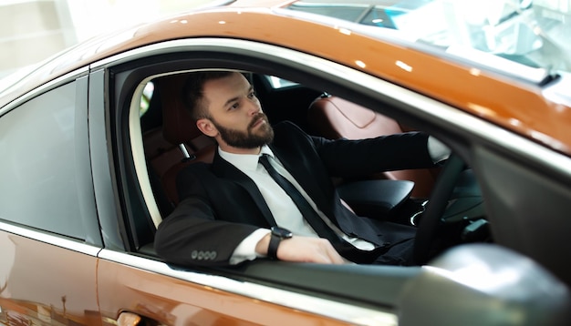 Foto ritratto ravvicinato di un bell'uomo d'affari barbuto elegante e fiducioso mentre guida la sua auto auto elettrica di lusso moderna