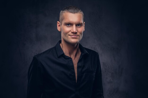 Photo close-up, a portrait of a handsome man in black shirt poses against a dark background, standing in the studio.