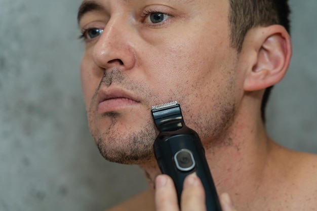 Close up portrait on handsome man shaving his beard by electric trimmer