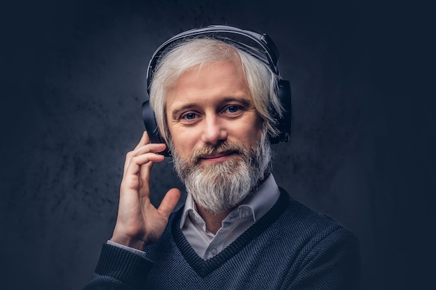 Close-up portrait of a handsome senior man listening to music in headphones. Isolated a dark background.