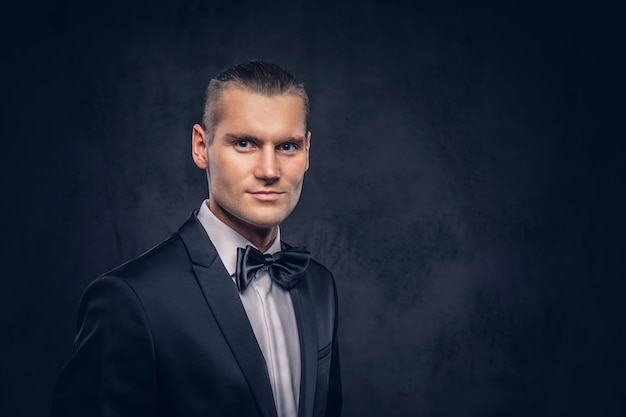 Close-up, a portrait of a handsome stylish man in an elegant black suit over a dark background.