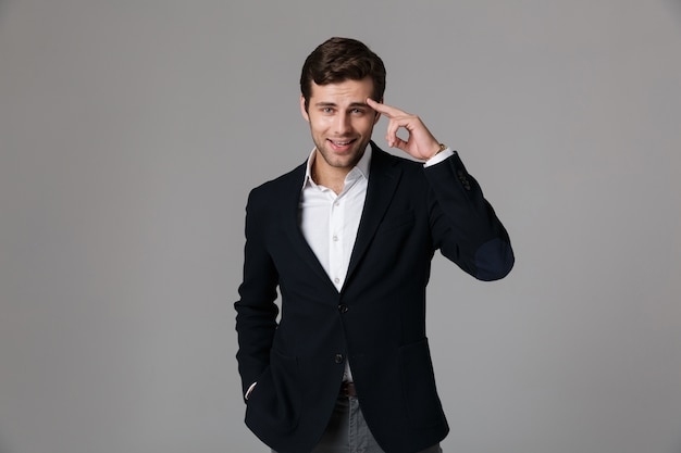 Close up portrait of a handsome young businessman dressed in suit isolated over gray wall, greeting someone