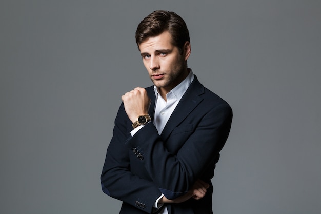 Close up portrait of a handsome young businessman dressed in suit isolated over gray wall