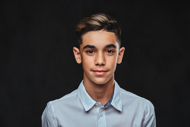 Close-up portrait of a handsome young guy with stylish hair dressed in a white shirt. Isolated on a dark background.