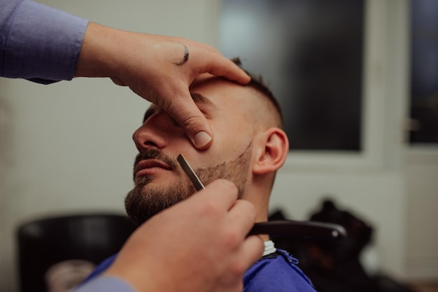 Close up portrait of a handsome young man getting beard shaving with a straight razor Focus on the blade Selective focus High quality photo