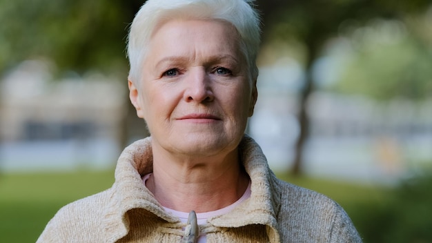 Close up portrait of happy aged beautiful female looking at camera relaxing posing outdoors in cool weather smiling senior woman elderly lady feeling positive enjoy retired carefree life concept