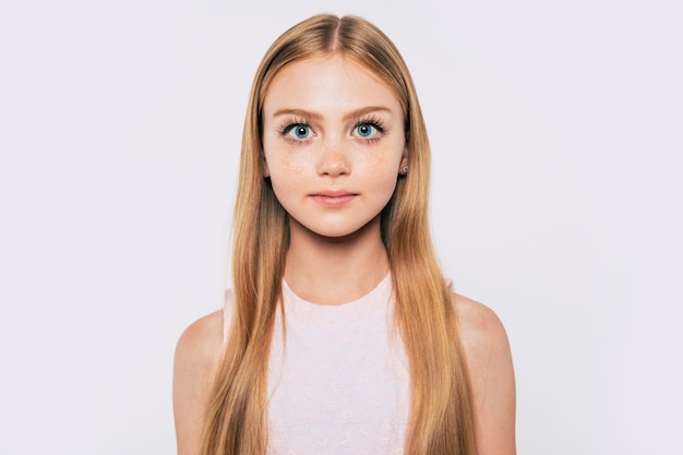 Close up portrait of happy attractive and cute blonde little girl with long hair while she is posing isolated on white background and smiling