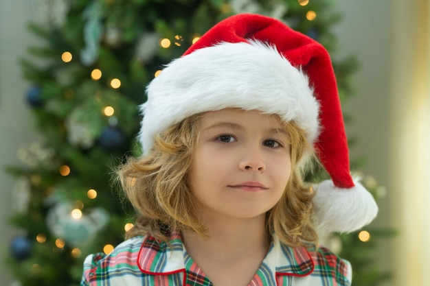 Close up portrait happy funny child in santa hat near christmas tree christmas and new year concept