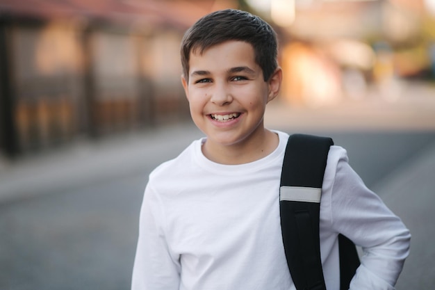 外のバックパックと白いスエット シャツで幸せな微笑んだ 10 代の少年の肖像画を間近します。