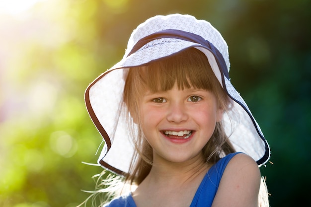 Close-up portrait of happy smiling little girl in a big hat. Child having fun time outdoors in summer.