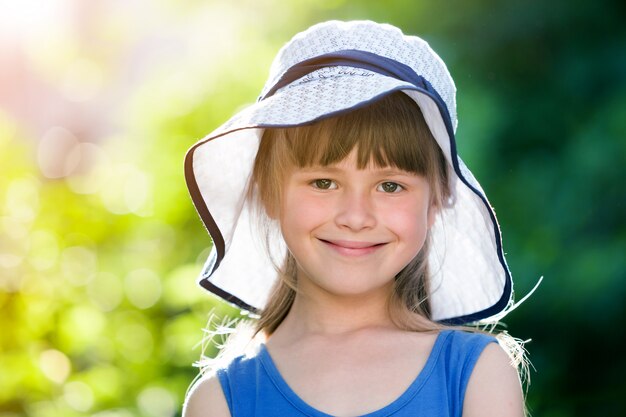 Close-up portrait of happy smiling little girl in a big hat. Child having fun time outdoors in summer.