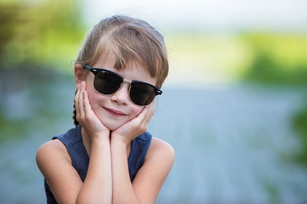 Close-up portrait of happy smiling little girl in dark sunglasses with long hair outdoors in summer.