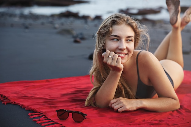 ビーチのビーチタオルの上に横たわって、水着で幸せな笑顔の女性のクローズアップの肖像画。