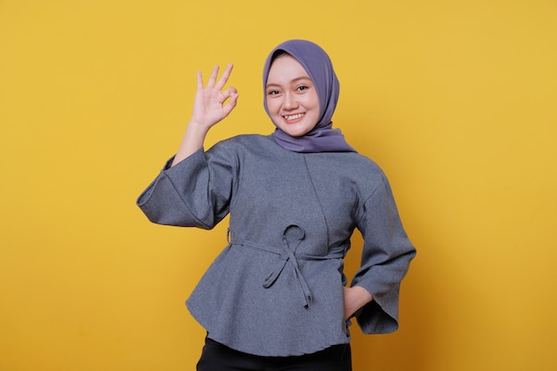 Close-up portrait of happy young asian woman wearing hijab showing saying okay gesture