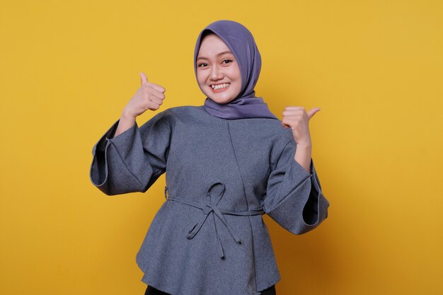 Close-up portrait of happy young asian woman wearing hijab showing thumb up gesture