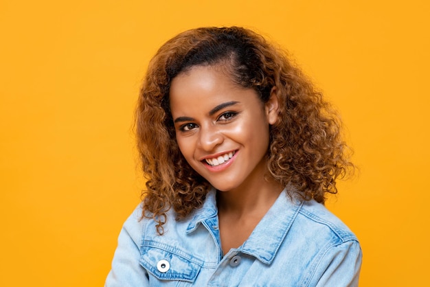 Close up portrait of happy young beautiful African American woman smiling while looking at camera in isolated studio yellow background