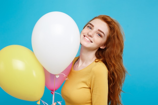 Close up portrait happy young beautiful attractive redhair girl smiling with colorful party balloon blue pastel wall