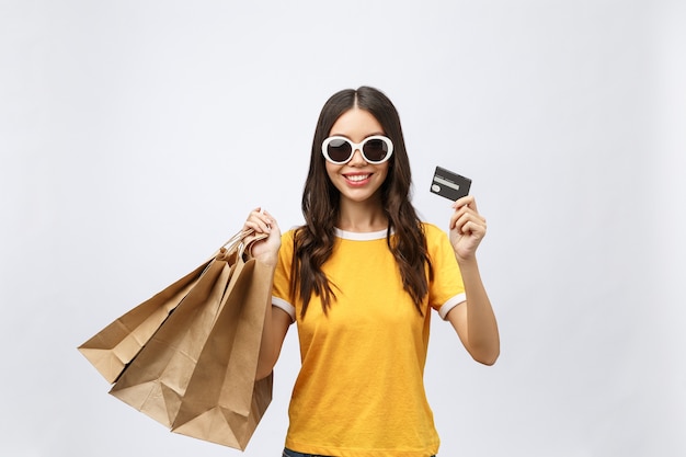 Close-up portrait of happy young brunette woman in sunglasses holding credit card and colorful shopping bags