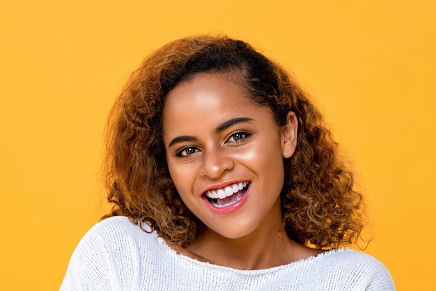 Close up portrait of happy young confident beautiful African American woman smiling and looking at camera in isolated studio yellow background