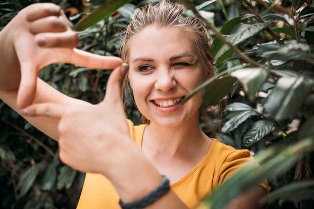 笑顔と指で写真を撮る幸せな若い女性のクローズアップの肖像画