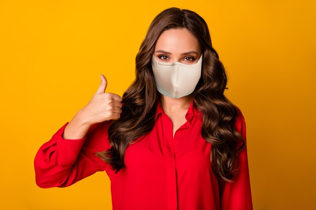 Close-up portrait of her she attractive gorgeous wavy-haired girl wearing safety mask showing thumbup mers cov insurance life health care isolated bright vivid shine vibrant yellow color background