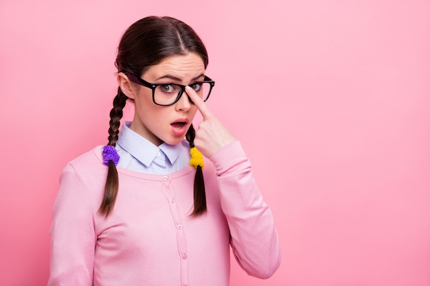 彼女の魅力的な素敵なかわいい面白い控えめな茶色の髪の少女のクローズアップの肖像画は、ピンクのパステルカラーの背景の上に分離された感動的な仕様の教育研究を身に着けています