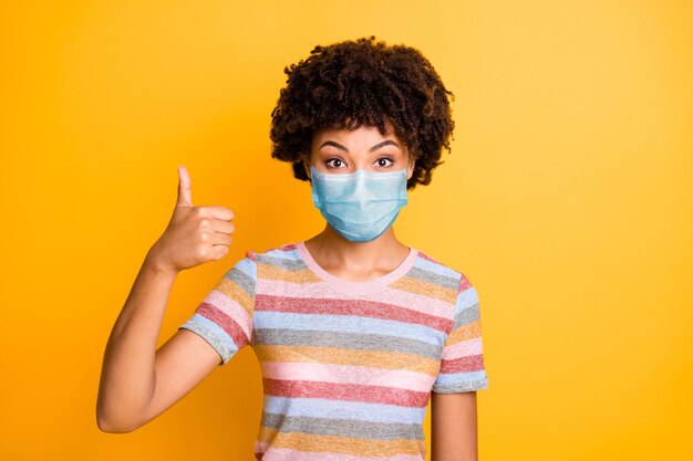 Close-up portrait of her she nice attractive healthy wavy-haired girl wearing safety gauze mask showing thumbup mers cov prevention isolated bright vivid shine vibrant yellow color background