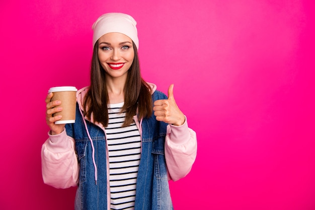 Close-up portrait of her she nice attractive lovely cheerful cheery girl holding in hands tea paper cup showing thumbup isolated over bright vivid shine vibrant pink fuchsia color