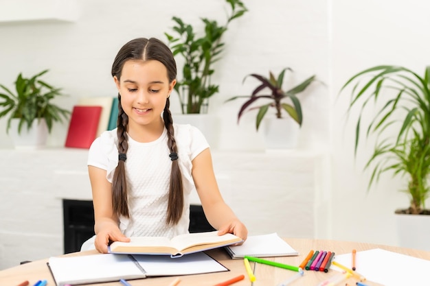 Close-up portrait of her she nice attractive pretty small little cheerful long-haired girl sitting table desktop writing article task homework in light white class room indoors.