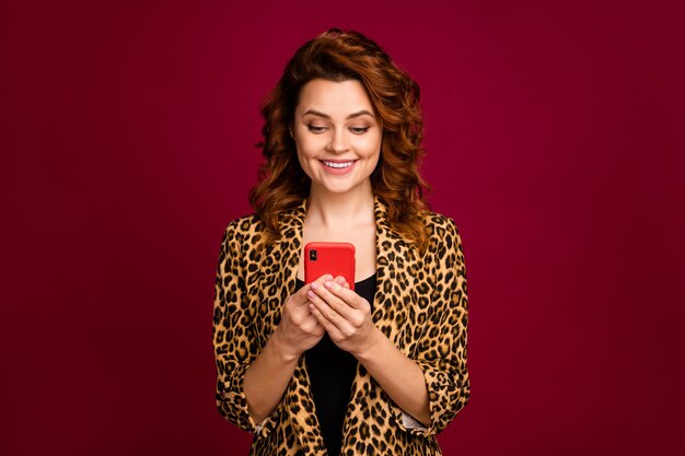 Close-up portrait of her she nice-looking attractive lovely charming cute cheerful focused wavy-haired girl using digital device isolated over red maroon burgundy marsala color background