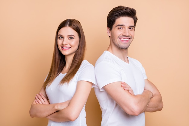 Close-up portrait of his he her she nice attractive cheerful cheery content successful couple wearing white t-shirt folded arms standing back to back isolated over beige pastel color background