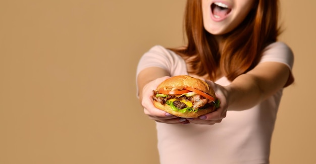 Close up portrait of a hungry young woman eating burger isolated over nude background