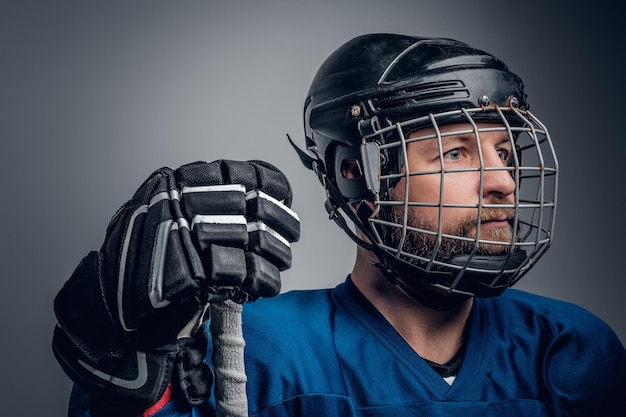회색 짤막한 배경에 안전 헬멧을 쓴 아이스하키 선수의 초상화를 닫습니다.