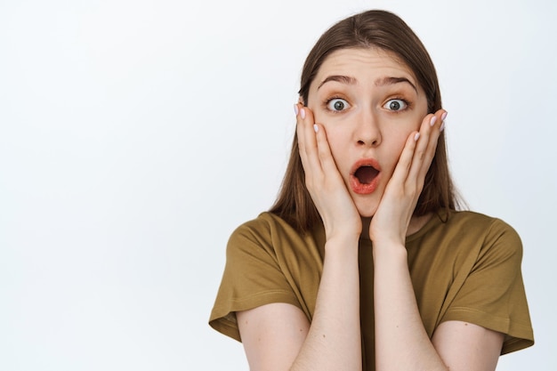 Close up portrait of impressed girl staring in awe, saying wow, looking at something amazing, standing on white