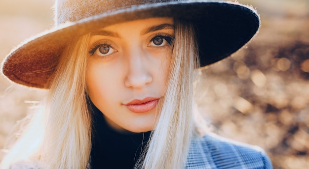 Close up portrait of a lady with blonde hair looking at camera while wearing a hat