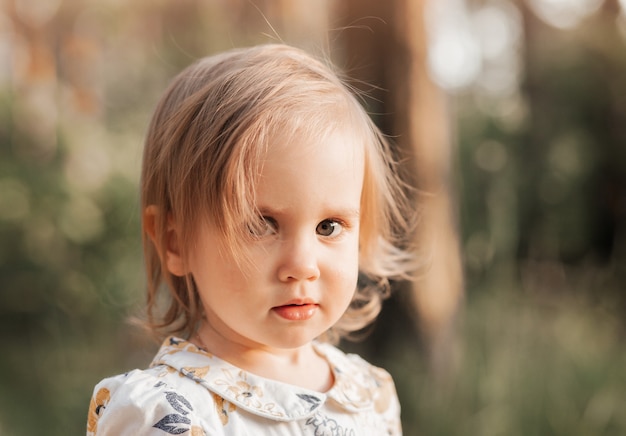 Close-up portrait of a little blonde girl in nature in the summer. Nature background.